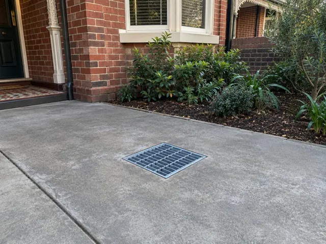 Concrete driveway with square drain grate outside a brick house in Crows Nest