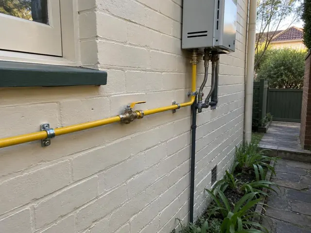 Yellow gas pipe and fittings on a painted brick exterior wall beside a window in Wollstonecraft